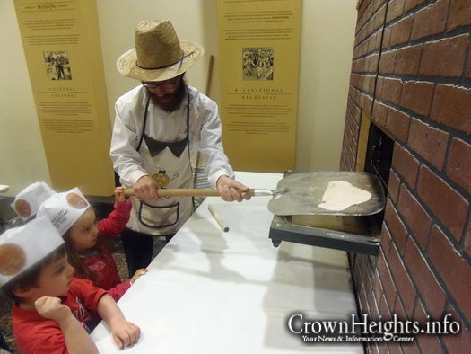 Jayden helps Rabbi Dovid Weinbaum of the Living Legacy remove the matzah she baked from the oven.
