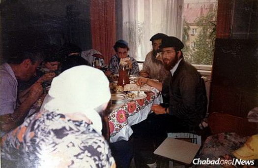 Rabbi Levi Heber, right, then 19, at the Moscow apartment where Genin performed circumcisions. The apartment belonged to an elderly woman known as Bubbe Charne, who would prepare a celebratory “feast” following each brit performed at her apartment. Genin can be seen partially obscured by Heber, the surgeon who worked with him is on the left, as Bubbe Charne approaches the table.