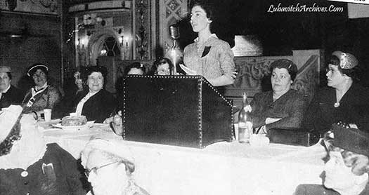 Rebbetzin Golda Schwei speaking at the Neshi Chanad Convention, with Rebbetzin Chana sitting to her right.