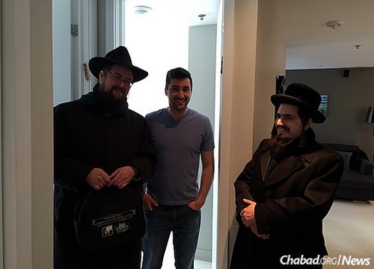 Winterfeld, left, and a Chassidic friend help David Prince, center, affix a mezuzah to the doorpost of his apartment.