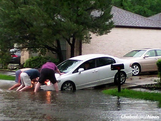 Community members help a neighbor push his flooded car out of the water.