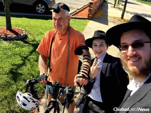 Mendel Greenberg helps a biker with tefillin, while Rabbi Ezra Wiemer, right, looks on.