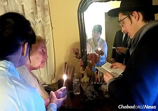 An elderly woman gets help lighting the menorah and reciting the Chanukah blessings.